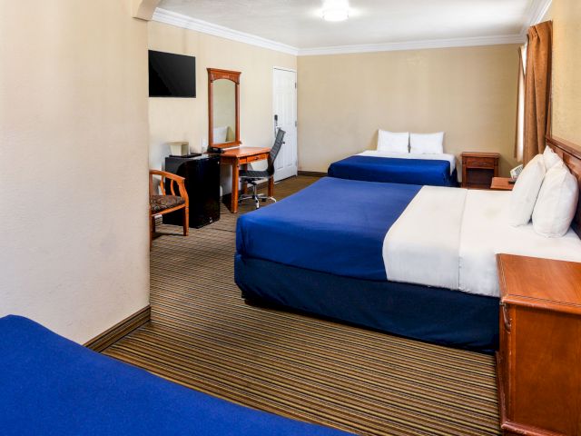 A hotel room with two queen beds, a desk, TV, and refrigerator.