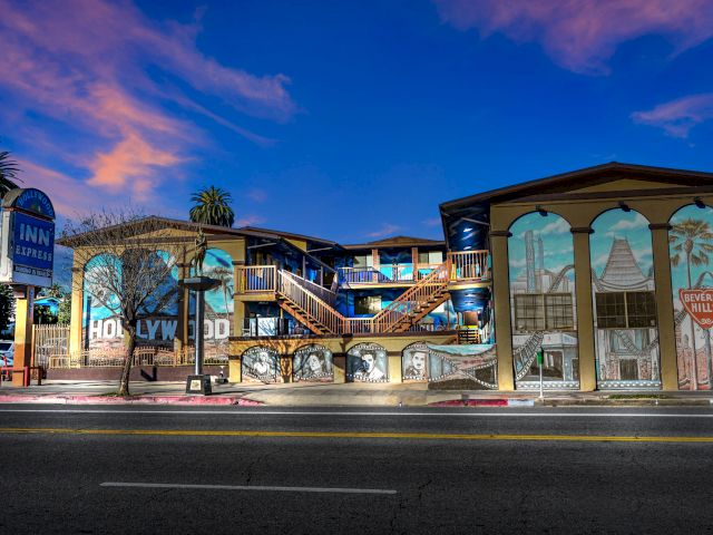 A two-story hotel building with a mural on the side, a staircase leading to the second floor, and a balcony.