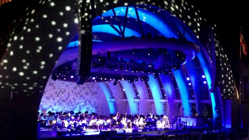 a large outdoor amphitheater with a blue and purple lit dome and a stage with an orchestra