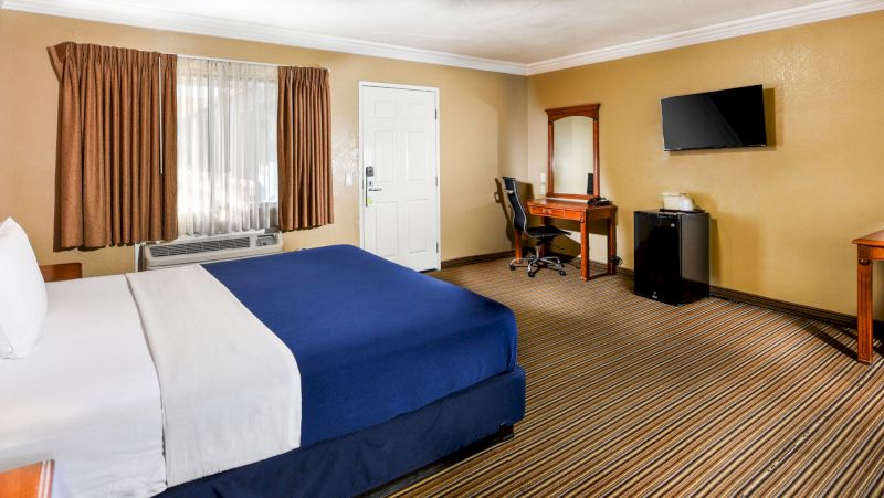 A hotel room with a bed, desk, TV, and window